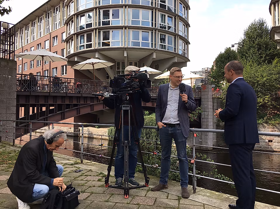 Interview mit Geschäftsführer Michael Otremba am Wasser, Kamerateam bei Dreharbeiten vor moderner Hamburger Architektur